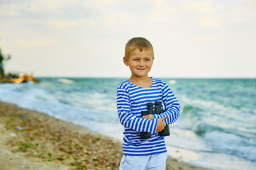 Fototapeta na wymiar The little boy in the vest with the binoculars , walks on the beach