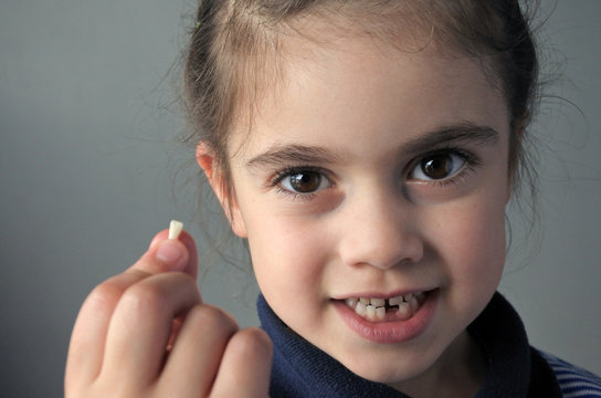 Proud young girl holds her first falling milk teeth