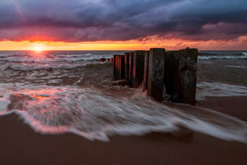 Right before sunset, the sun came out from the clouds. Its rays highlight the low ?umulus. Last sunbeams put colored gleams on the breakwater and on the waves of the Baltic Sea, Russia, Curonian Spit