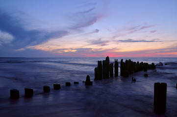 Silhouette old wooden breakwater panels at Curonian spit against the background of colorful twilight sky with cirrus clouds, Russia, Kaliningrad
