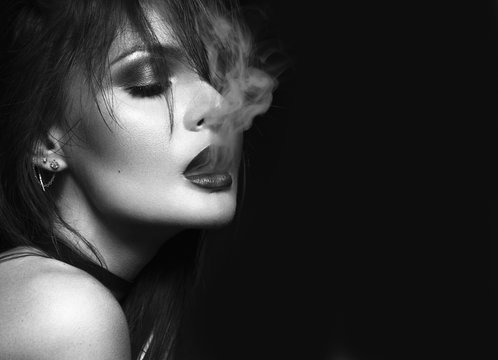 Beautiful sexy brunette girl with bright makeup, red lips, smoke from mouth. beauty face. Black and white