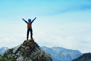 Obraz premium cheering successful woman backpacker open arms on mountain peak