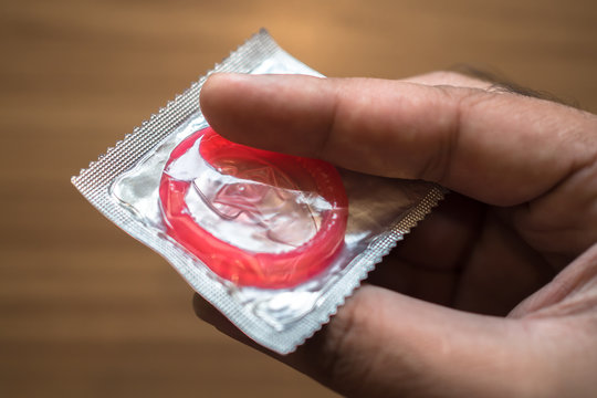 sealed condom in hand on wooden background
