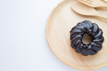 A chocolate glazed donut on wooden plate. Shot from above on a white background.