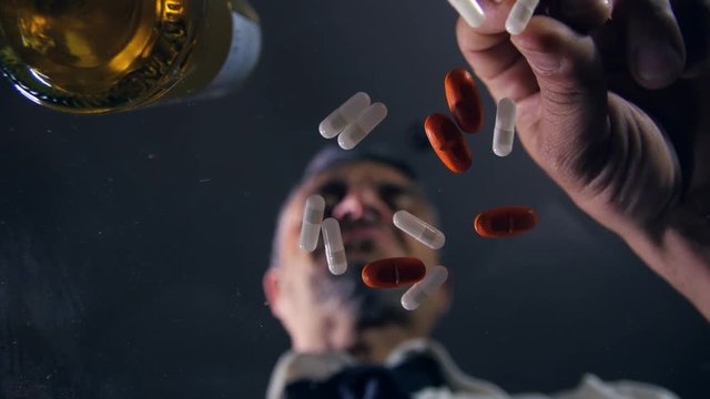 depressed man taking overdose of pills and drinking alcohol on a glass table as seen from below the glass,drug addiction concept