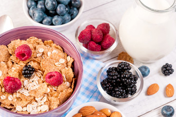 healthy breakfast with cornflakes berries, milk and almond nuts on wooden table