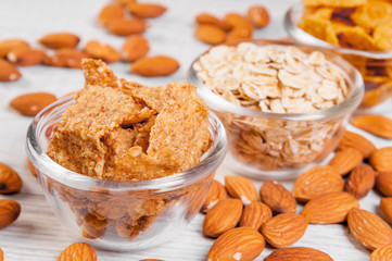assortment breakfast cereals in small glass dishes on wooden table, almond nuts close-up