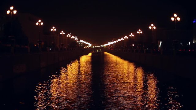 The glare of the lights on the water of the city canal at night