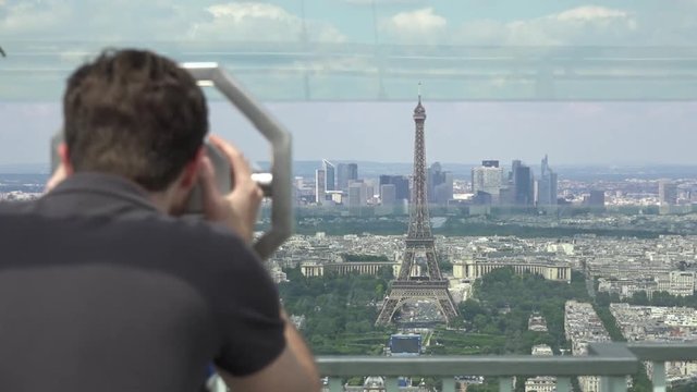 Male Tourist Watches Eiffel Tower Through Telescope, Paris. The Montparnasse Tower Panoramic Observation Deck has the most beautiful view of Paris.