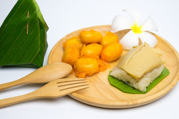 Thai Bean and Egg Yolk Dessert (Met Khanoon: THAI Dessert )and sticky rice and egg custard creamy wrapped banana leaf, on a wooden plate.