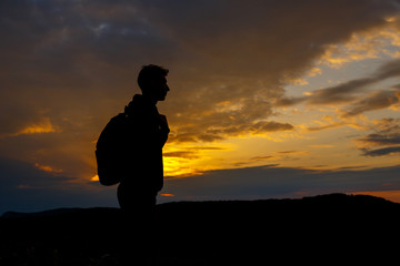 Silhouettes of hiker with backpack enjoying sunset view from top of a mountain