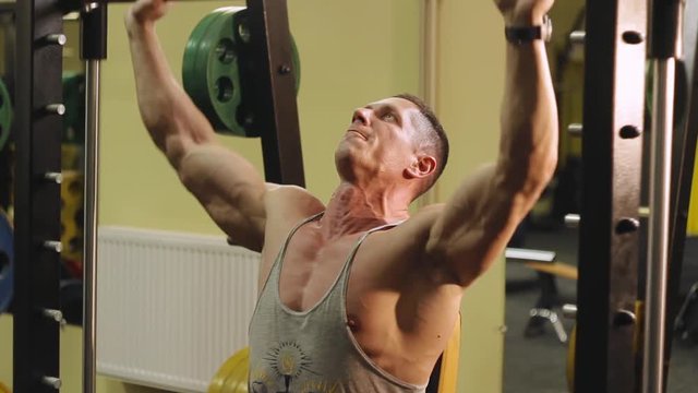 The man pumps his neck muscles and arms with the help of trainer at the gym sequence