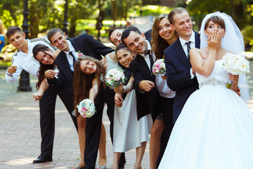 Bride closes her mouth with a palm while groom and friends look