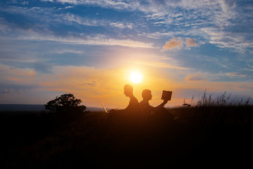 Fototapeta premium silhouette of a men with laptop and a book on sunset or sunrise background