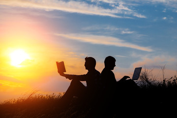 Fototapeta na wymiar silhouette of a men with laptop and a book on sunset or sunrise background