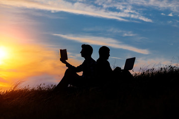 silhouette of a men with laptop and a book on sunset or sunrise background