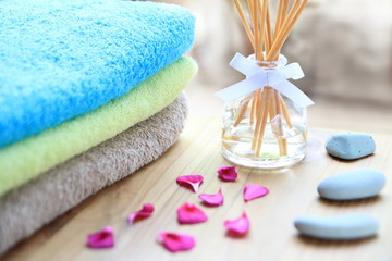 Aromatherapy reed diffuser bottle on a wooden table with towels, petals and massage stones