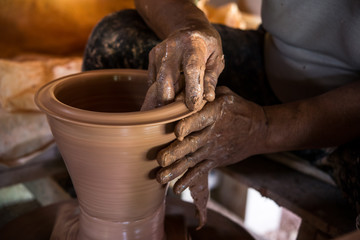 Old potter creating a new ceramic pot on pottery wheel