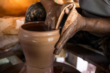 Old potter creating a new ceramic pot on pottery wheel