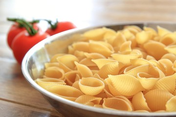 Dry conchiglie pasta shells in a stainless steel bowl with vine tomatoes in the blurred background