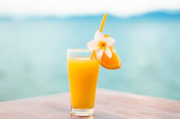 glass of orange juice, decorated with tropical plumeria flower on the beach
