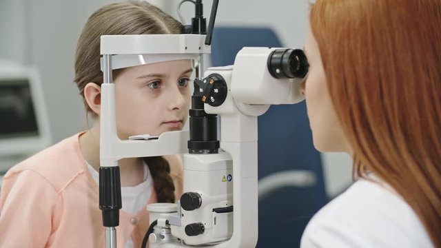 Closeup of female pediatric optometrist examining eyes of little girl with biomicroscopic slit lamp device