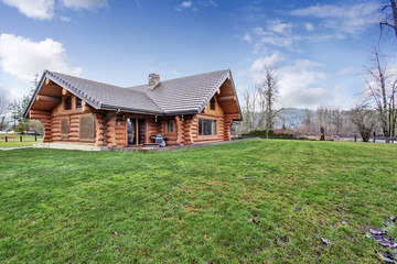 Fototapeta na wymiar Large log cabin house exterior with grass filled back yard.