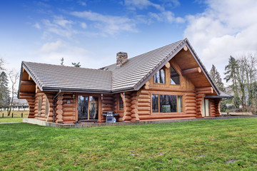 Fototapeta na wymiar Large log cabin house exterior with grass filled back yard.