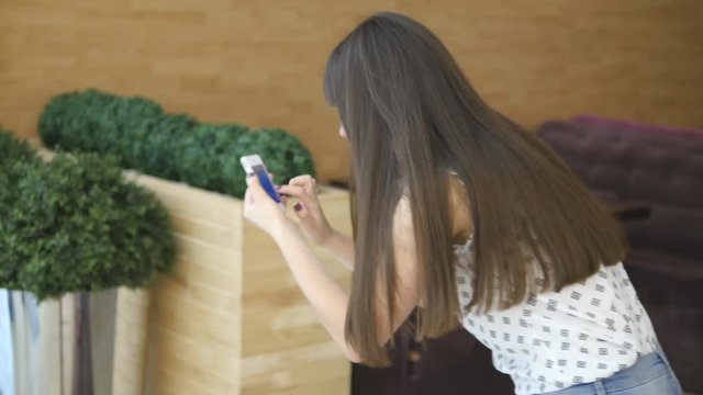 Young woman playing indoor at shopping center, using smart phone. Girl play the popular smartphone game