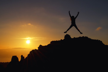 Junge Frau springt bei einem Sonnenuntergang auf einem Berg vor Freude im Urlaub in die Luft
