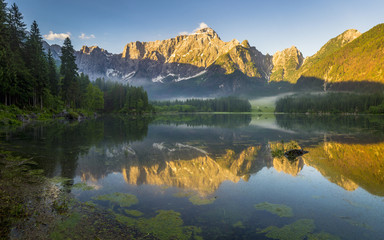 Oświetlone szczyty Alp wschodzącym słońcem nad górskim jeziorem w Alpach Julijskich,Włochy