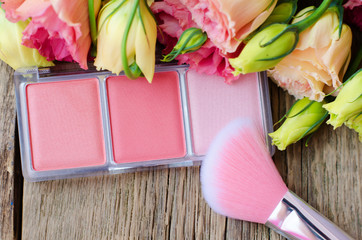 Obraz na płótnie Canvas Blush and brush for blush on a wooden table next to the flowers close up. Women's cosmetics