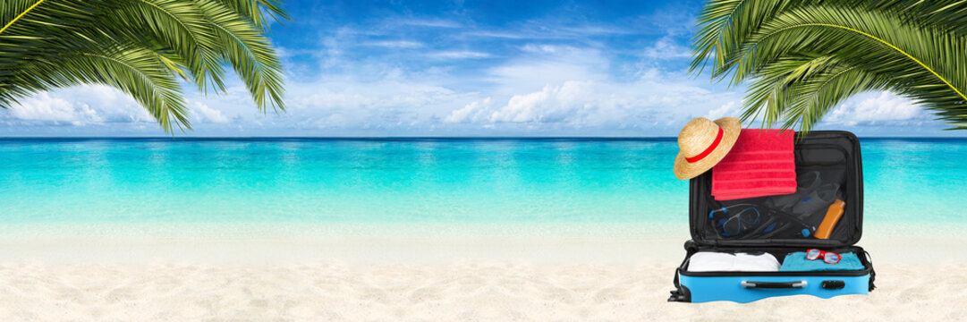 open suitcase on tropical paradise beach background with turquoise blue water coco palms and blue sky / Paradies Traumstrand Hintergrund mit Reisekoffer Palmen und blauem Himmel