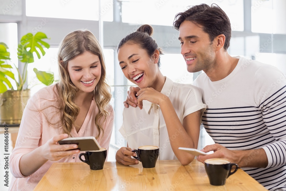 Poster group of friends using mobile phone while having cup of coffee