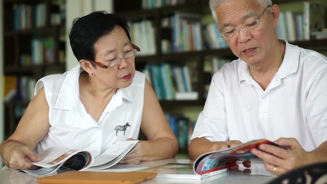 Asian senior couple reading books and magazines together in small library. Learning and study concept
