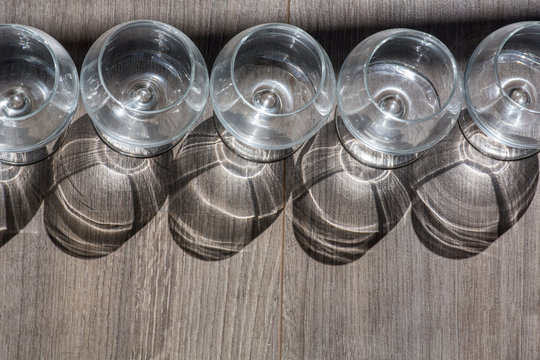 Row of five cognac glasses with shadows on the brown wood