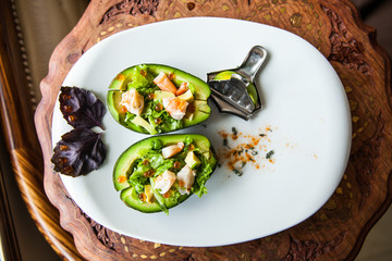 Avocado salad with prawns on white plate on wooden table