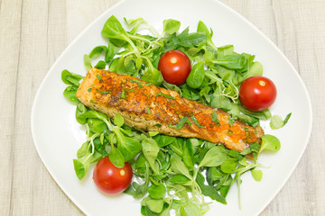 Roasted salmon with roots and tomatoes on a white plate