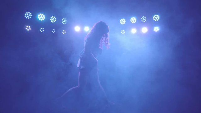 Silhouette of woman solo freestyle performance dancing barefoot on a dark stage with blue lights and smoke