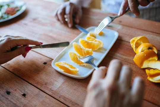 Hands of two persons eating orange slices with cutlery