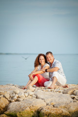 Fototapeta na wymiar Cute Couple Sitting on Rocks at the Beach