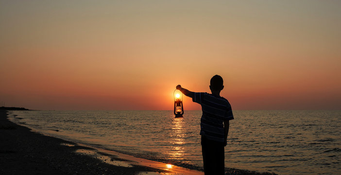 Young boy with lamp at sunrise on the beach