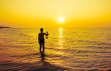 Fototapeta na wymiar Young boy with lamp at sunrise on the beach