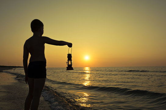 Young boy with lamp at sunrise on the beach