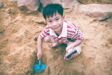 Fototapeta premium Top view. Adorable asian boy has fun digging in the sand on a summer day.