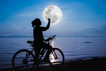 Silhouette of happy female celebrating with arm up towards the full moon