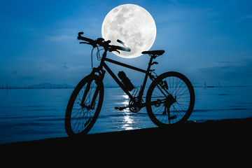 Fototapeta premium Silhouette of bicycle on the beach against beautiful full moon.