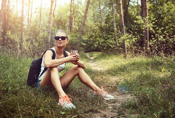 Young active woman hiker resting in the wood, drinking coffee in the morning. Concept of travel, adventure and lifestyle.  