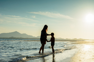 Silhouette of mother and son at tropical beach during sunrise