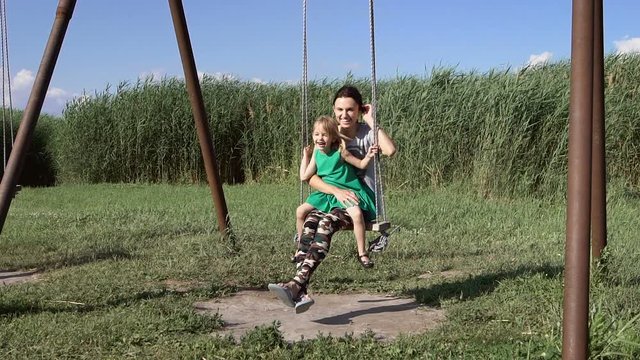 Beautiful young woman with a charming little girl swinging outdoors